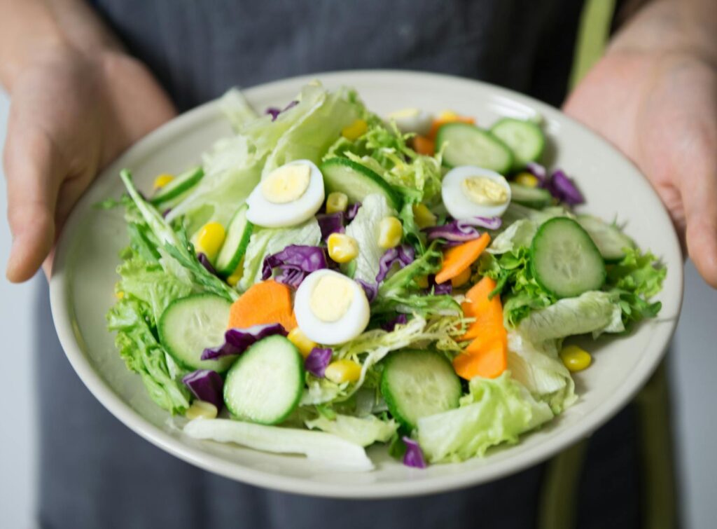 Freshly prepared salad with cucumber, lettuce, carrots, and egg slices presented on a plate.