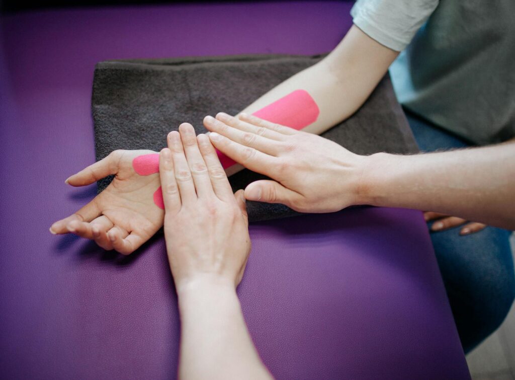 Close-up of hands applying pink kinesiology tape during a relaxing arm massage.